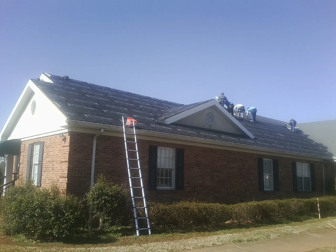 Crew tearing shingles off a brick ranch roof with a ladder set — Emergency Roof Repair work by our crew in Garrison