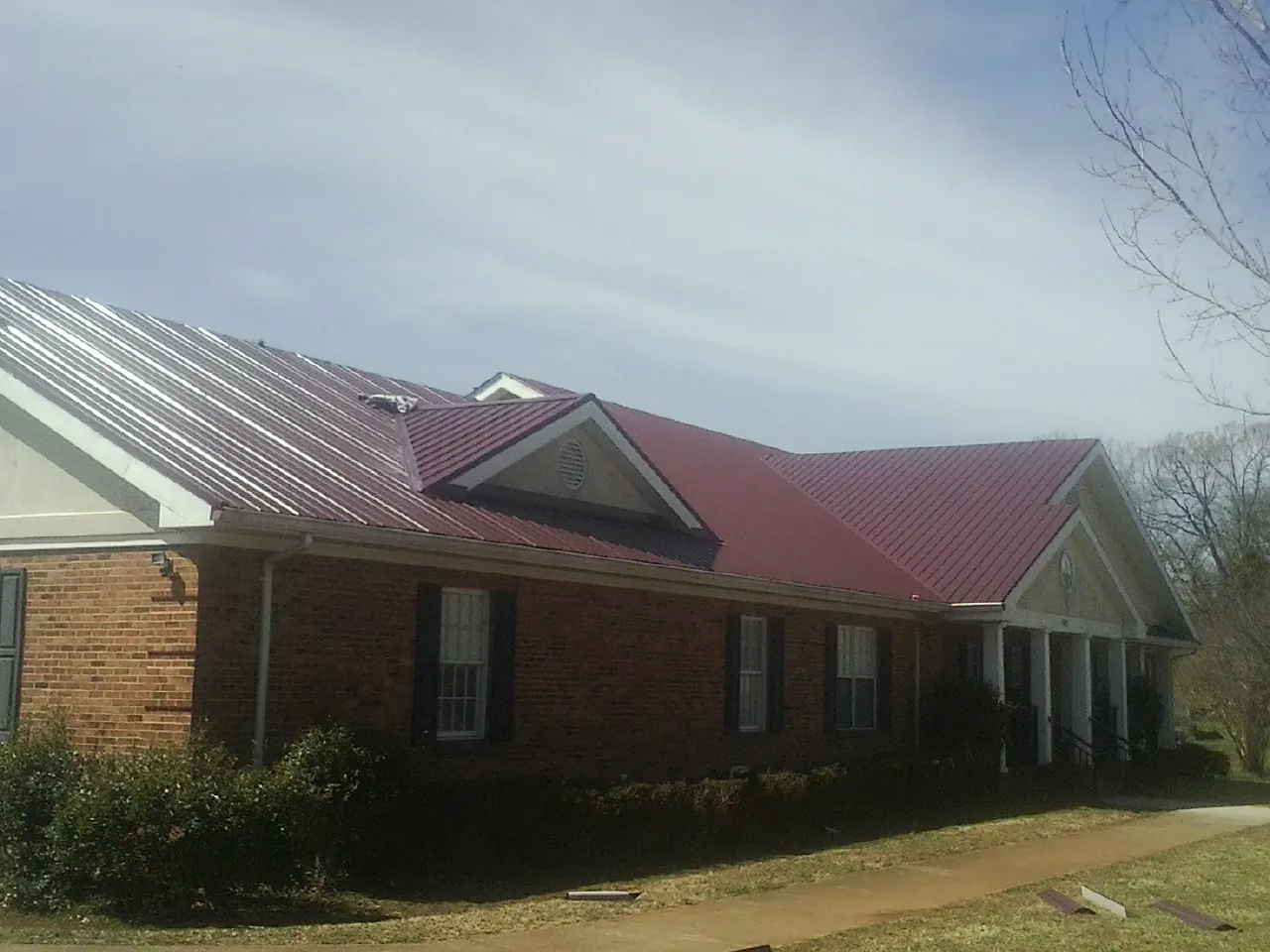 Red metal roof with gabled entries on a long brick building, from a Hail Damage Roof Repair job in Garrison