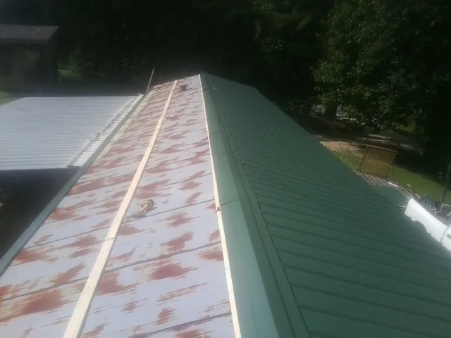 Old rusted panels beside newly installed green metal roofing — Wind Damage Roof Repair by Roofing Brothers in Garrison