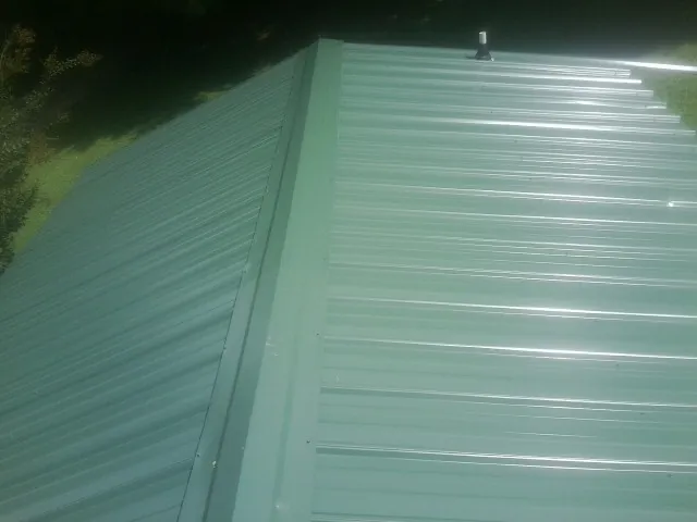 New green metal panels meeting at the ridge of a roof — Flat Roof Repair work by our crew in Garrison
