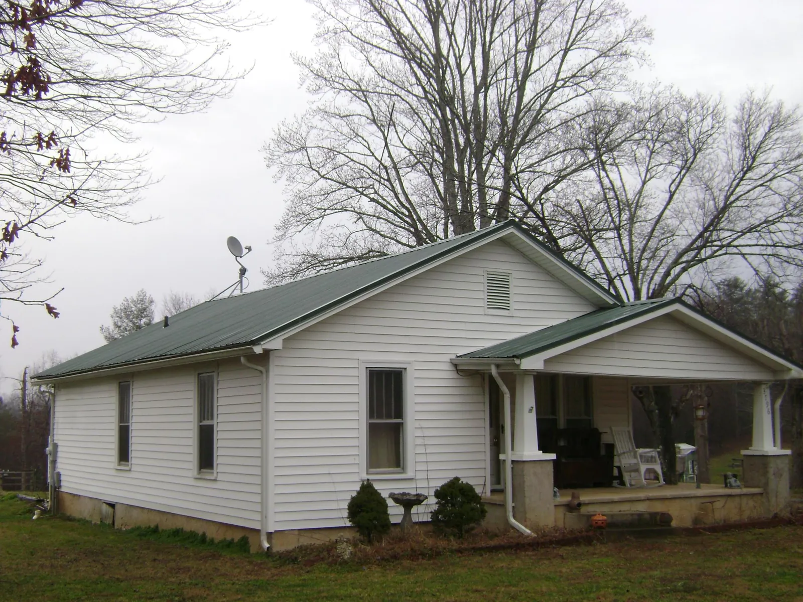 Green metal roof on a white bungalow with a side porch in Garrison